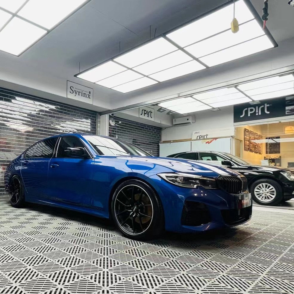 Blue car in a showroom with various brand logos on the walls.